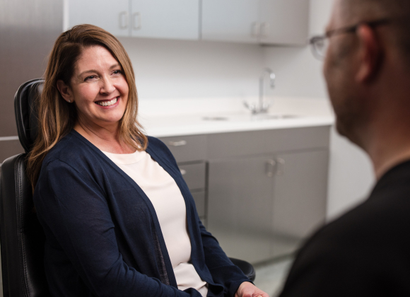 patient sitting in a dental chair smiling while talking to an oral surgeon