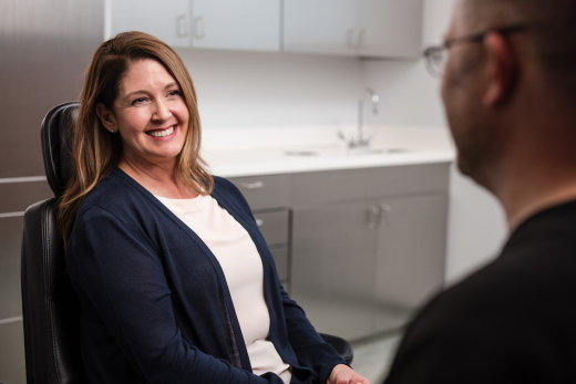 patient sitting in a dental chair smiling while talking to an oral surgeon