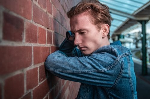 young man leaning against brick wall